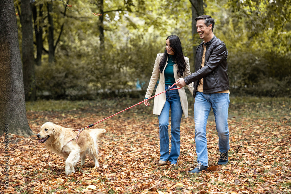 Fototapeta premium A joyful couple strolls through a vibrant autumn park with their golden retriever, enjoying the beautiful fall scenery together.