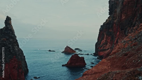 Red volcanic rocks and sharp sea stacks along madeira island portugal captured in wide shot above atlantic waters