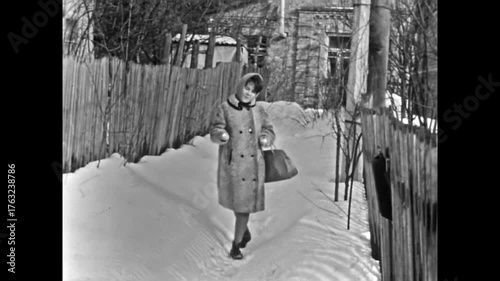Woman in coat walking along snowy village street on sunny winter. Out-of-town New Year. Bright sun in Christmas archive holiday joy. Sunlight on snow drifts. Vintage old film. Archival retro 1960s