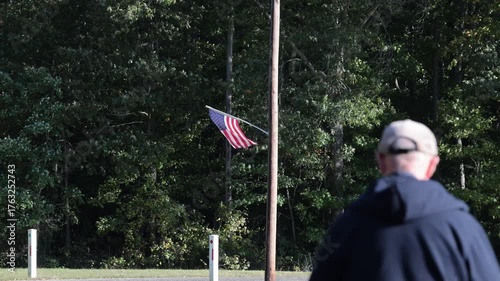 Leonardtown, Maryland USA A man walks on a large field beneath an American flag flying from a telephone pole.  