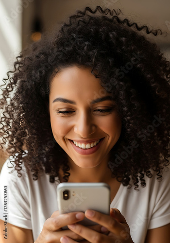 Smiling woman with curly hair using a smartphone indoors casual setting close-up