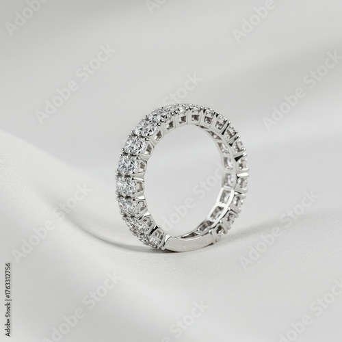 Close up view of a silver eternity ring with diamonds on a white surface in soft lighting