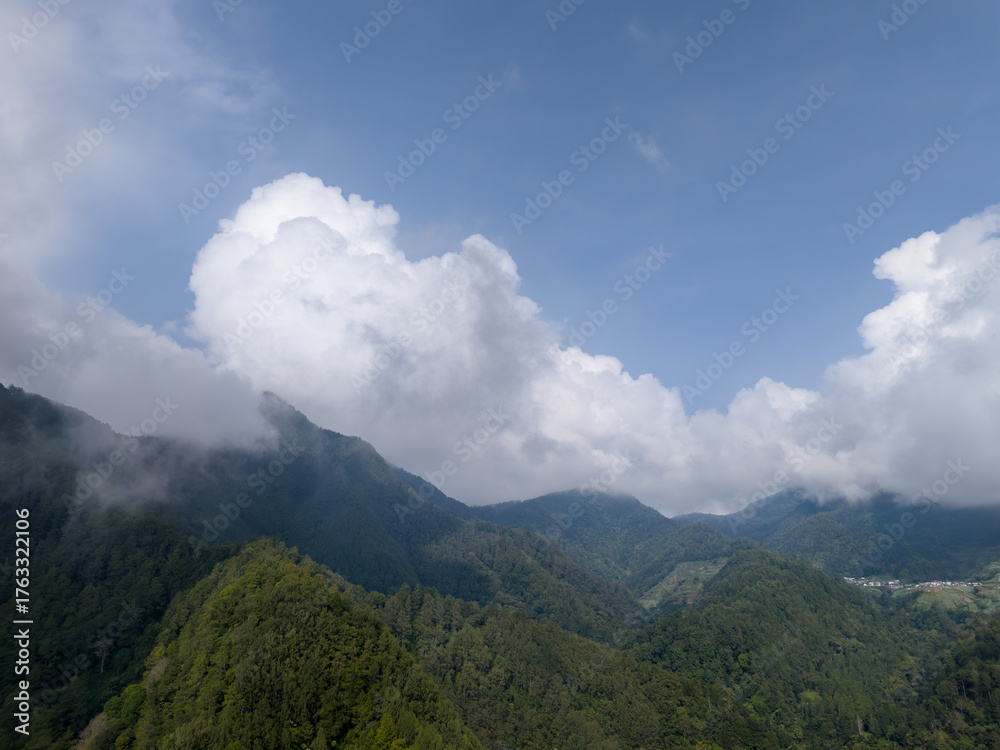Obraz premium Aerial view of green mountain landscape with clouds and blue sky.