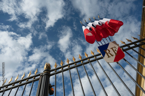 Flags of France fly at the Prefecture, catching the sunlight against a backdrop of clouds. The scene showcases national pride and the beauty of the location.