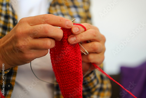Knitting process of red fabric with needles, close-up of hands with yarn. Concept of hobby, creativity and coziness.
