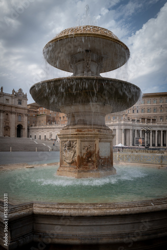 Historic stone fountain with flowing water in a grand European square on a cloudy day.