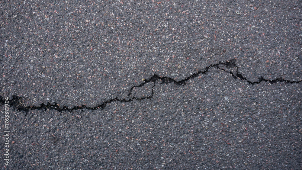 Obraz premium Asphalt on the road with a prominent crack. The textured surface conveys wear, weathering, and the need for maintenance in urban infrastructure. Road damage
