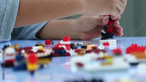 Children hands play with colorful lego blocks on white table.
