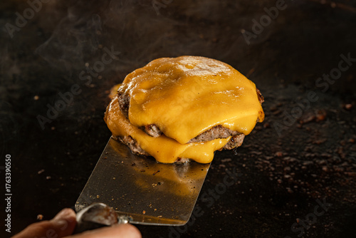 A stack of double juicy hamburger patties layered with melted cheddar cheese, freshly lifted off the flat griddle