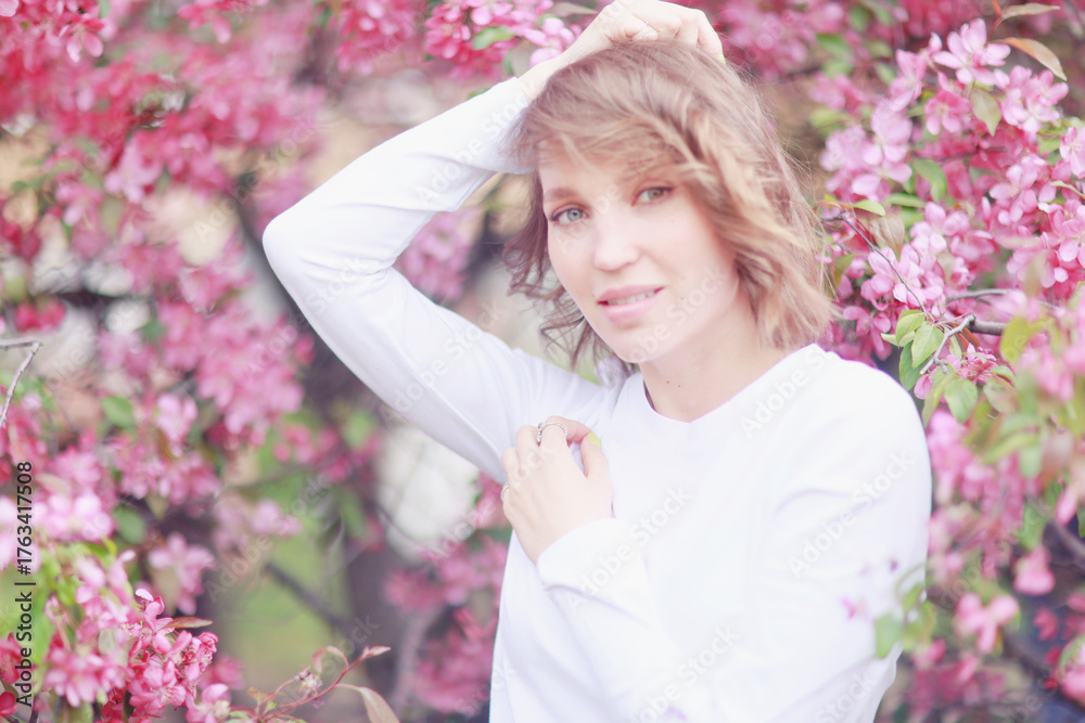 Fototapeta premium Springtime background, a woman in pink in a blooming cherry orchard, a model posing in a romantic style