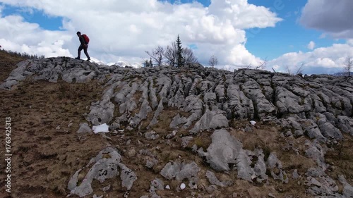 A hiker navigates rocky terrain surrounded by stunning mountain views and dynamic cloud formations. Experience the natural beauty of outdoor exploration.