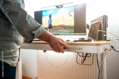 Man raising standing desk in bright office.