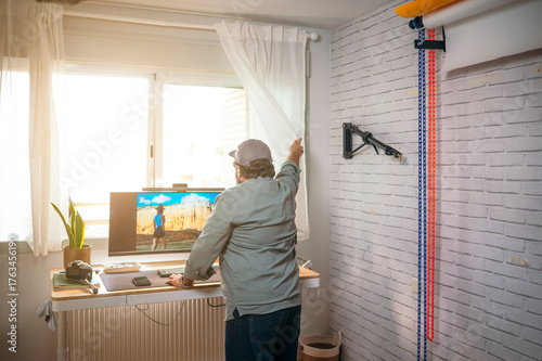 Man opening curtain beside standing desk.