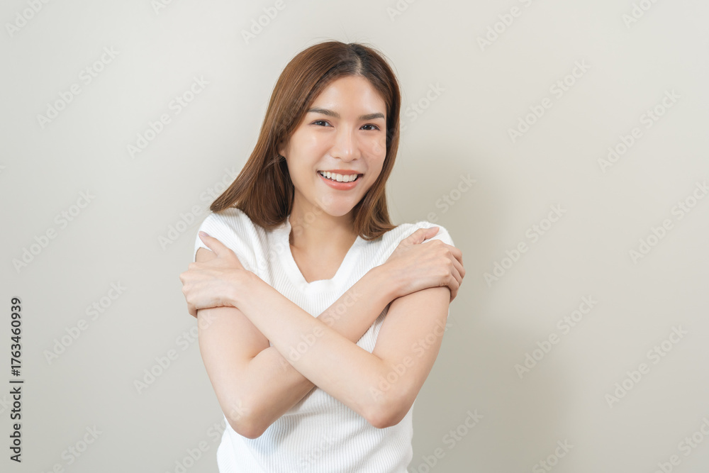Fototapeta premium Smiling positive, hug self care happy asian young woman hands hugging herself shoulders, enjoy yourself, self love and self care, smile girl face expression self esteem standing isolated on background
