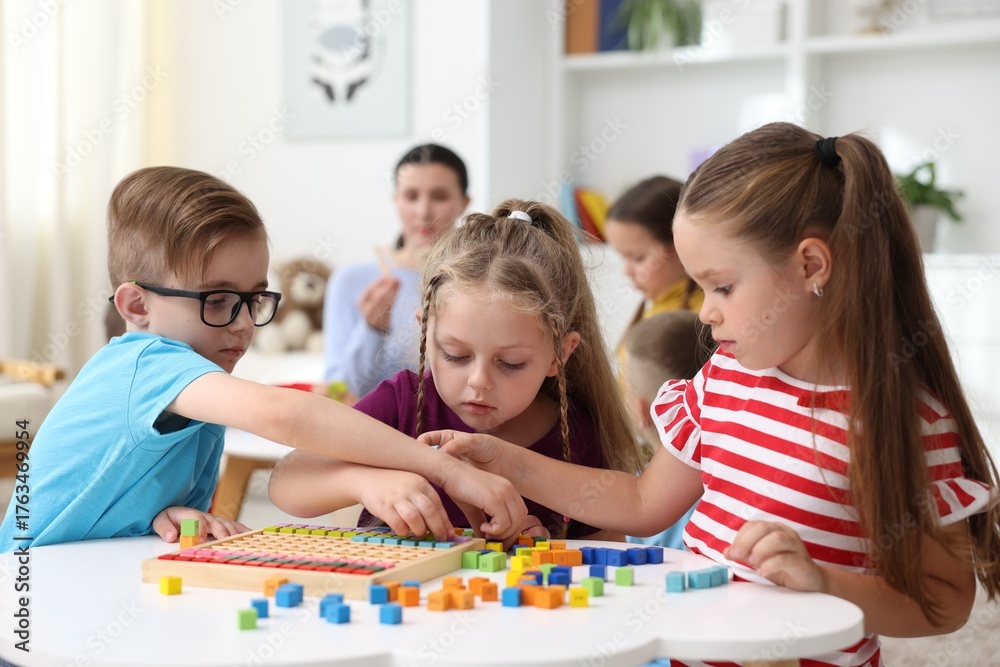 Fototapeta premium Cute children and teacher at white tables during lesson in elementary school