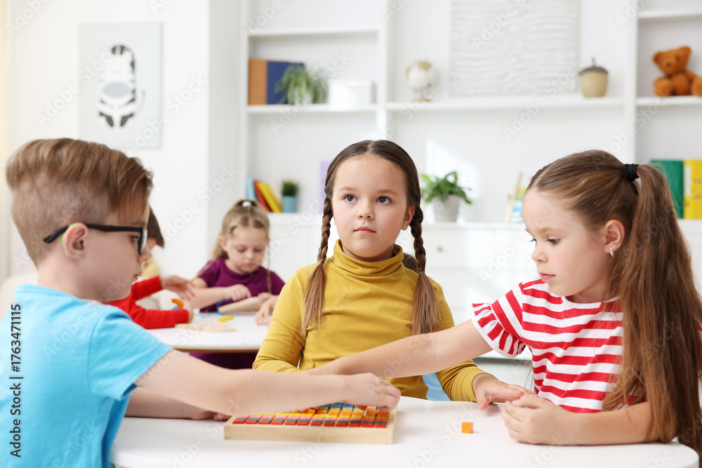 Fototapeta premium Cute children at white tables during lesson in elementary school