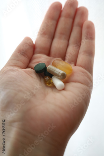 Close up of hand with various pills and capsules on white background. Dietary supplements and vitamins, treatment topic, pharmaceuticals, health improvement, vitamin deficiency in the human body.