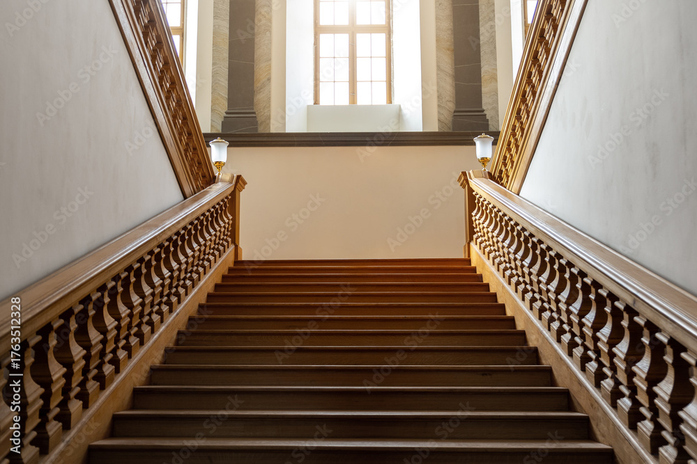 Obraz premium Elegant wooden vintage empty staircase rises toward large bright windows filled with warm light. Symmetrical balustrades and refined craftsmanship convey timeless elegance and architectural harmony