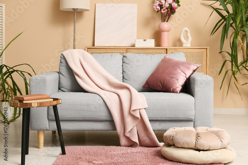 Grey sofa with coral cushion and plaid near beige wall in interior of living room