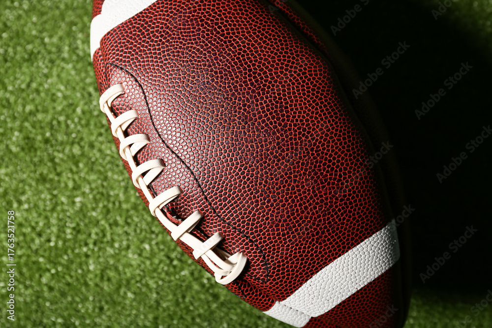 Obraz premium American football ball on green grass as background, closeup