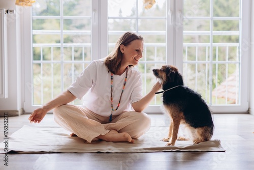 Middle aged woman practices Kundalini yoga at home with her dog nearby. Spiritual balance, feminine energy, harmony, mindfulness, and emotional wellness with animals