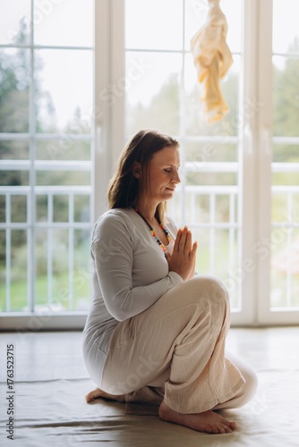 Calm woman practicing kundalini yoga at home in prayer pose. Mindfulness, inner peace, and healthy lifestyle in serene morning light