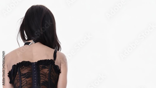 Upper-body back view closeup of a dark brunette woman wearing black lace corset, isolated on white copy-space background.