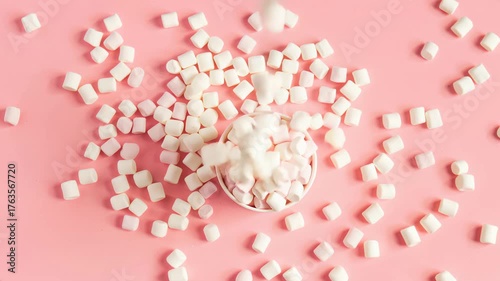 Marshmallows falling into a cup on a pink background during a fun, creative food project.