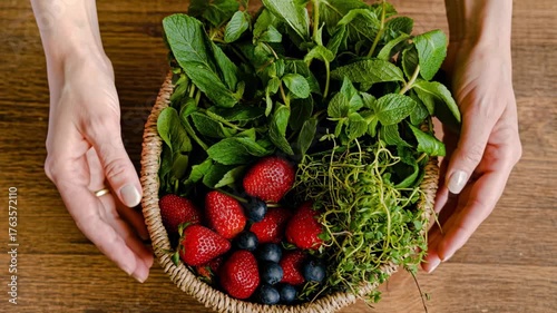 Holding a basket filled with fresh herbs and berries on a wooden table. 