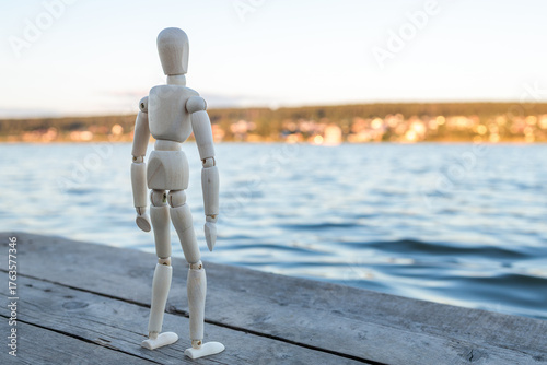 A white figure stands on a wooden pier overlooking a body of water