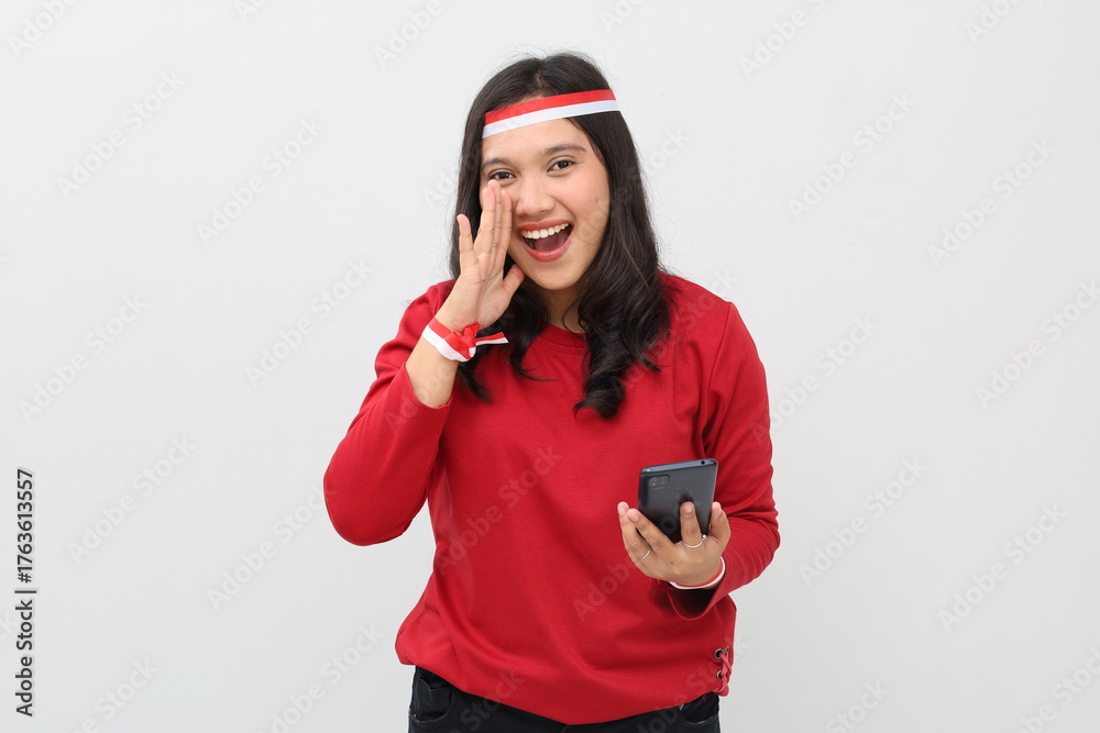 Naklejka premium Indonesian woman with red and white ribbon to celebrate Indonesian independence day holding mobile phone while making hand gestures of announcement or promotional advertisement.