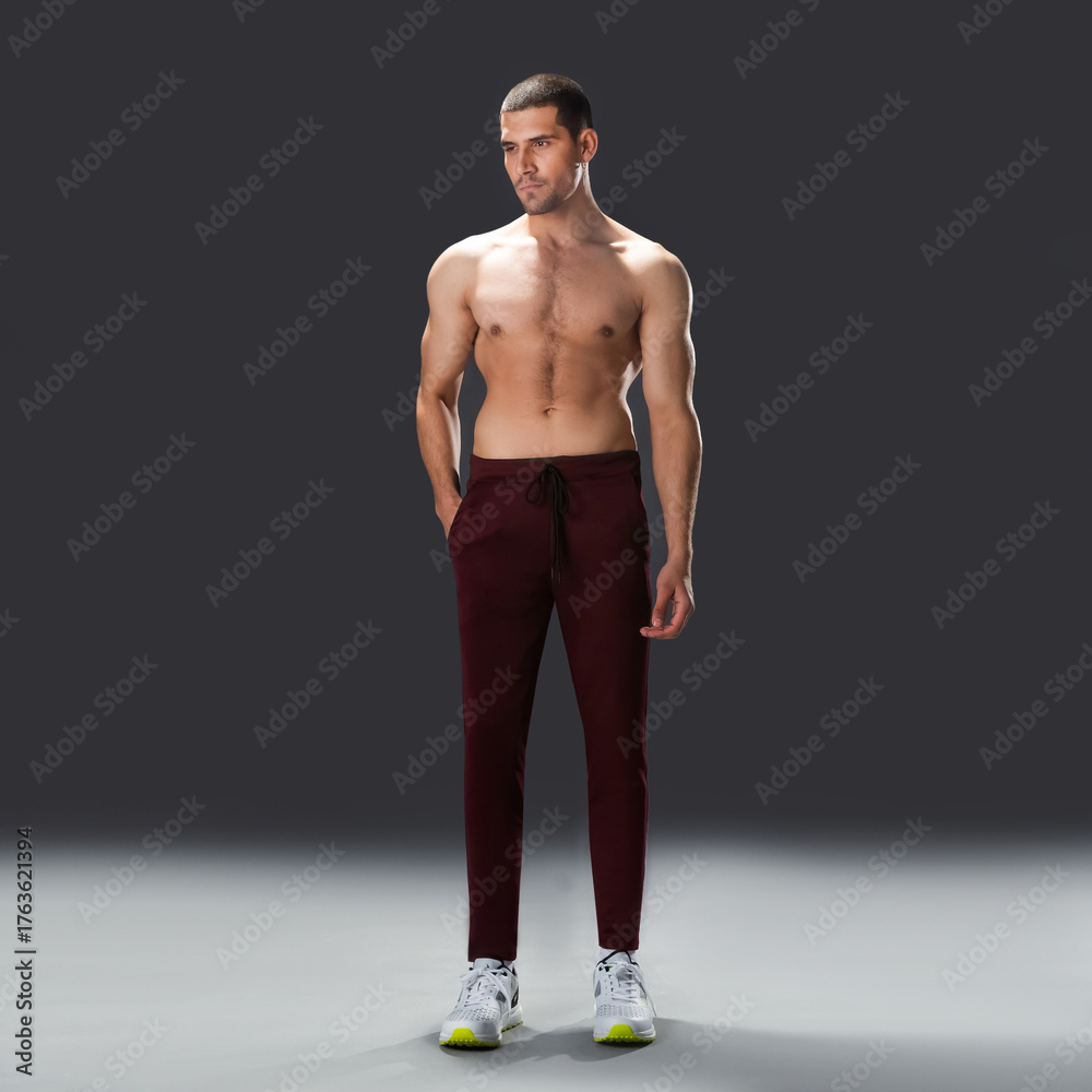 Fototapeta premium Shirtless athletic male model standing in studio, showcasing muscular physique, fitness body, and healthy lifestyle on dark background.