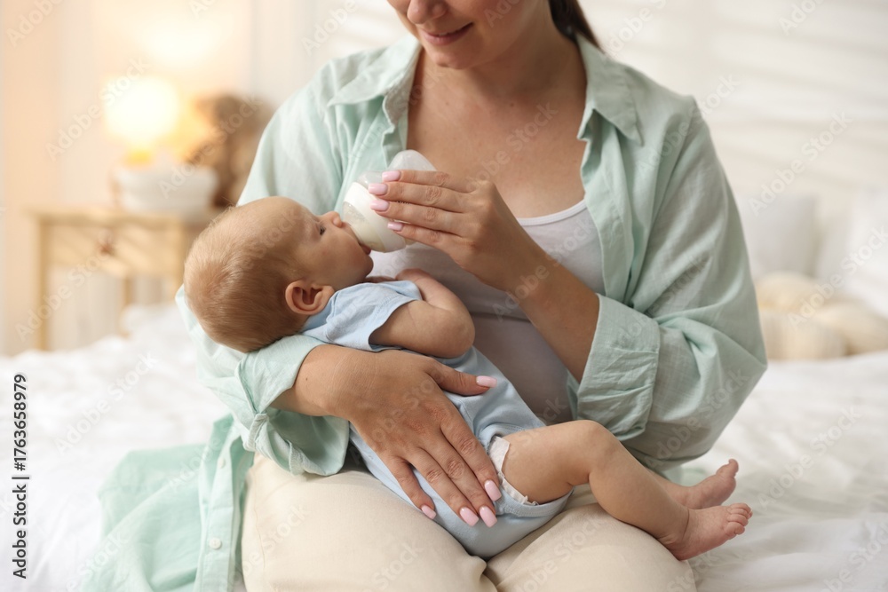 Obraz premium Mother feeding her newborn baby with bottle on bed at home, closeup