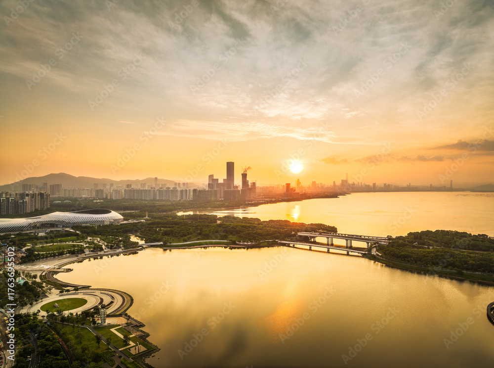 Fototapeta premium Aerial view of the modern city skyline with commercial buildings and green park along the bay at golden sunrise in Shenzhen.
