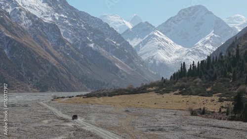 Vehicle moves steadily across rocky terrain, showcasing the vast landscape of majestic mountains and lush greenery, with a gradual camera pan enhancing the scene's depth and beauty