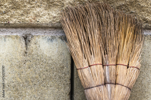 Broom made of straw leaning against stone wall. Traditional craft, rural life, and eco-friendly cleaning tools.