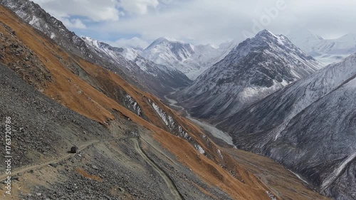 Scenic mountain landscape features a winding road and a vehicle navigating through rugged terrain, showcasing the dramatic contrast of snow-capped peaks and autumn foliage, camera pans across