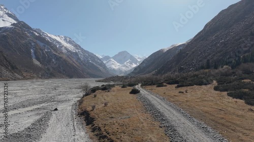 Scenic mountain valley features a winding road leading through rocky terrain, with majestic peaks in the background, as the camera pans to capture the expansive natural beauty and tranquility