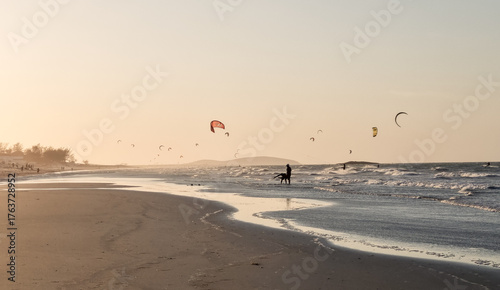 Evening kitesurfing session at golden hour, silhouettes riding waves while the sky glows. Tranquil coastal setting with a soft tropical breeze.