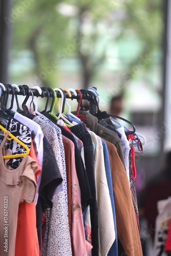 Feira de Second Hand ao Ar Livre na Rua, Moda Circular e Economia Circular, com Luz Natural, Arara Vertical Cheia de Cabides e Roupas Coloridas, Imagem Vertical
