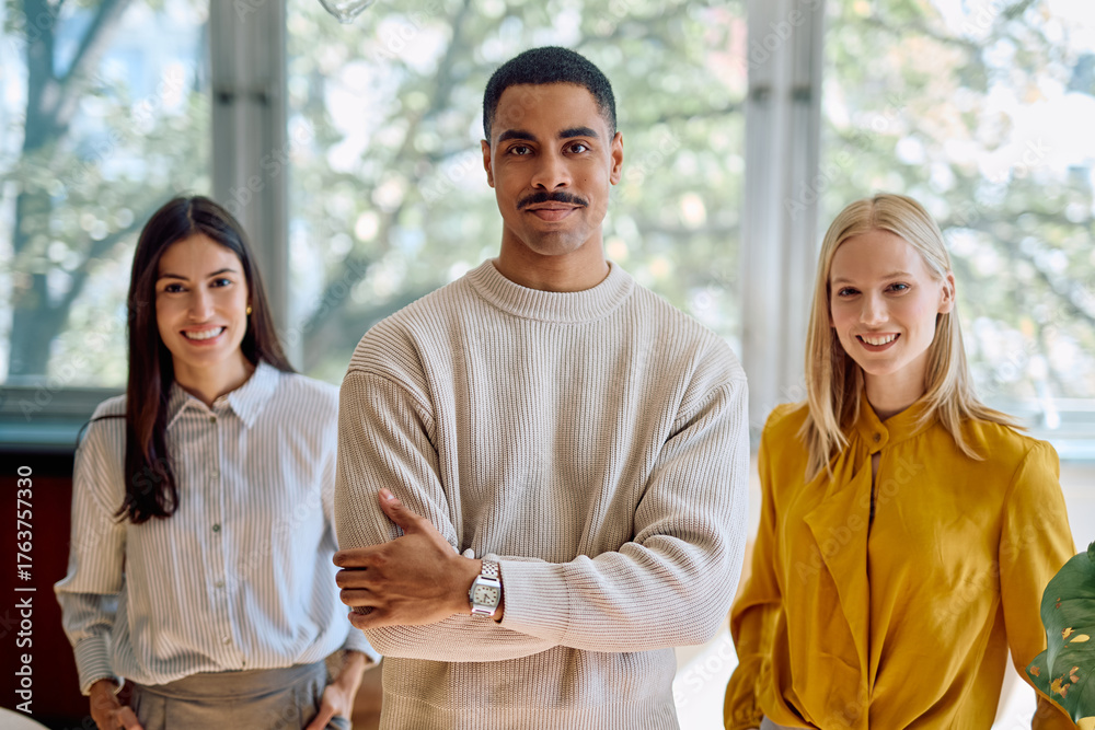 Naklejka premium Diverse co-workers smiling at camera, showing teamwork, confidence, and professionalism in a contemporary office setting