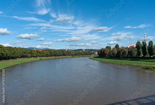 The Uzh River in the summer greenery of its alleys of Linden and Chestnut hides the city of Uzhhorod under a blue sky with white clouds.