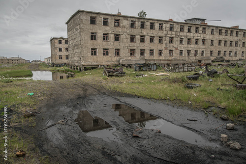 Quadro su tela Crumbling Russian apartment blocks with shattered windows and overgrown grass in Ugolnye Kopi, Chukotka, Russia, under cloudy summer skies
