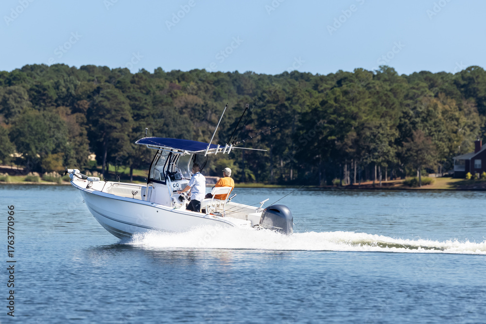 Obraz premium Fishermen on center console fishing boat enjoy summer day on the lake. Power boat cruising on freshwater lake.