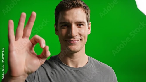 Young Man in Gray T-Shirt Making an OK Gesture with Hand in Front of Bright Green Screen Background for Creative Media Projects, Promotional Content and Professional Visuals