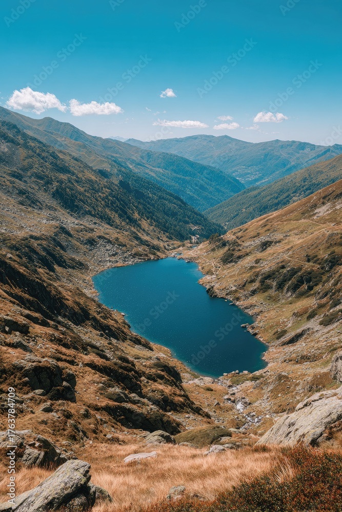 Naklejka premium A mountain lake nestled in a valley, surrounded by peaks and clear blue skies
