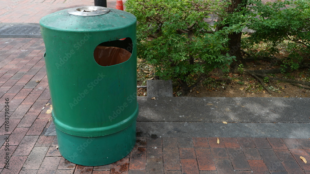 Obraz premium Green trash bin with built-in ashtray for smokers to dispose of ash or cigarette waste, placed outdoors in a public area for cleanliness and waste management.