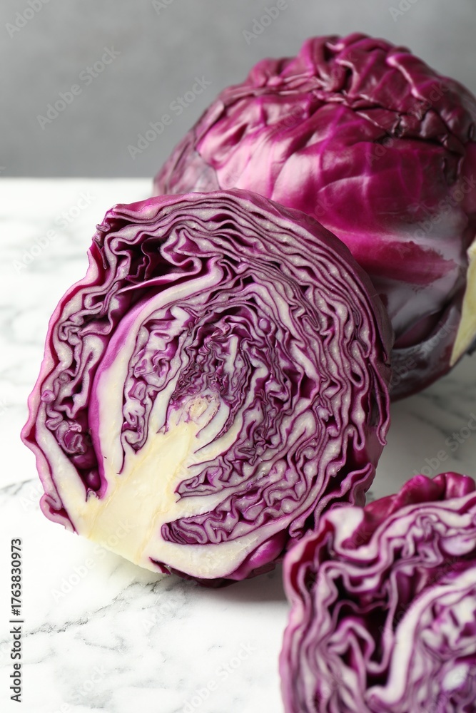 Obraz premium Whole and cut red cabbages on white marble table, closeup