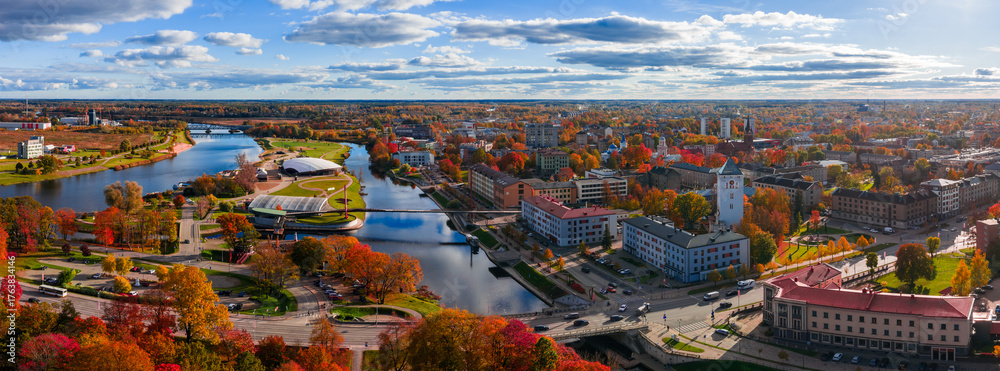 Obraz premium Aerial view of Jelgava, Latvia, with Lielupe and Driksa rivers, Holy Trinity Church tower, Culture Center, and autumn parks under crisp light and clouds.