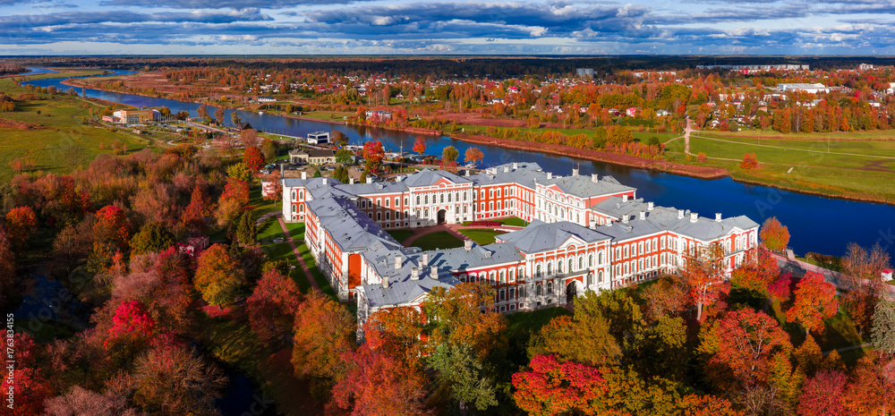Obraz premium Aerial view shows Jelgava Palace in Jelgava, Latvia, beside the Lielupe River, U shaped plan, courtyard, fall trees, low rise skyline, meadows, crisp light, dramatic clouds.